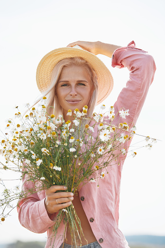 Beautiful woman in hat and with a basket of field daisies in sunny summer day