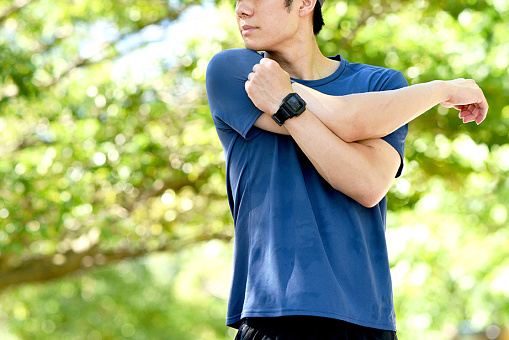 Young Asian man wearing sportswear doing warm-up exercises outdoors