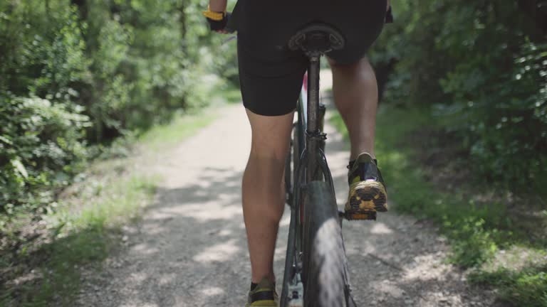 A man riding a mountainbike on a path through a lush green forest. Mountain biker in nature. Abstract lower close up back tyre view. Recorded with cinema camera.