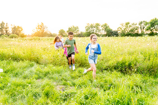 A small group of school aged children are seen running across the grass as they play at recess.  They are each dressed casually and are smiling as they enjoy the fresh air.