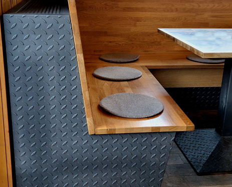 a bench seat in a restaurant. side panels made of non-slip sheet metal in a gray industrial design. wooden seat and table. circular pads. dining room, fitted