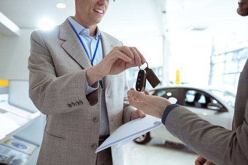 Cropped close shot of happy salesman giving car key to the customer in car showroom