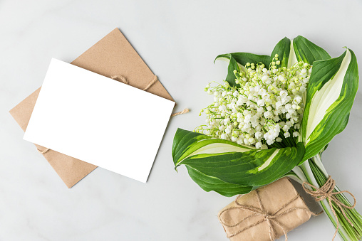 Blank greeting card with Lily of the valley flowers bouquet and gift box on white background. Wedding invitation. Womens day, Valentines day card. Mock up. Flat lay.