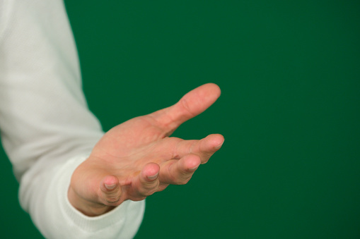 Empty hand palm up gesture, isolated man guy on a green background chromakey close-up dark hair young man. white sweatshirt