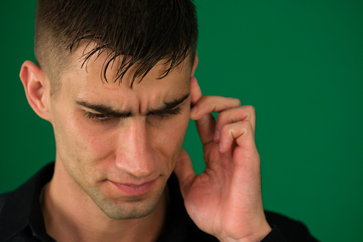 emotions of a handsome man guy on a green background chromakey close-up dark hair young man. My head wont stop throbbing