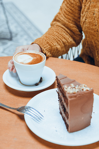 vertical image of unrecognizable woman eating cake and drinking coffee, for social networks of cafe and pastry concept