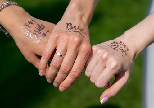 three hands of the bride's friends crossed with each other with the inscriptions bride on a background of grass