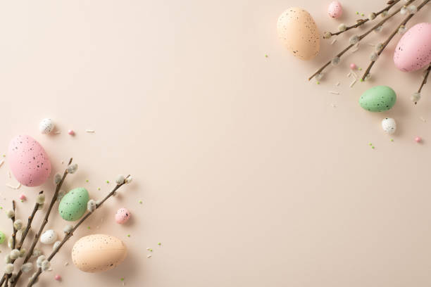 istock Easter elegance captured in single frame. Top view vibrant eggs, graceful pussy-willow twigs, sprinkles create picturesque scene on pastel beige background. Ideal for your custom text or advertisement 1909720875