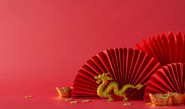 istock Festive Lunar New Year setting: side view table adorned with feng shui essentials, gold coins, dragon figurine, and fans on a vibrant red backdrop. Empty space for text 1909720884