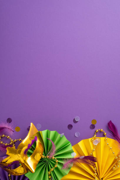 istock Masquerade Marvel: vertical top view luxe Venice mask, traditional beads, feathers, confetti, energetic fans arranged on mesmerizing purple backdrop, forming alluring composition with space for ads 1909721400