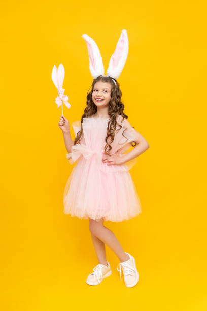 istock Happy children's Easter. A curly-haired girl dressed in an Easter bunny. An extraordinarily beautiful teenage girl with long ears and a lush dress on a yellow isolated background. 1909757474