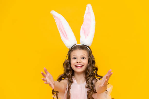 istock Happy Easter. A little girl dressed as a rabbit celebrates a spring holiday. A charming, smiling child in a beautiful dress with long ears on a yellow isolated background. 1909766461