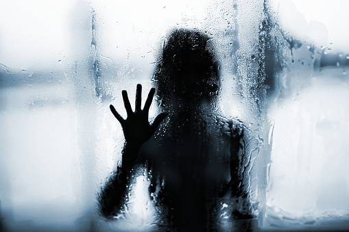 Contours of a woman behind wet glass