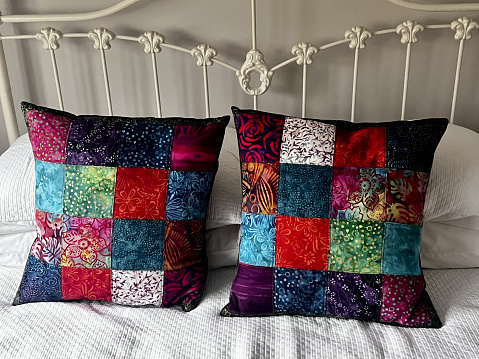 Colourful patchwork cushions made from batik fabrics. Placed on a metal bed