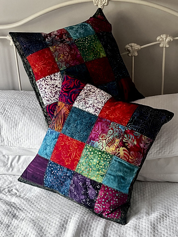 Colourful patchwork cushions made from batik fabrics. Placed on a metal bed