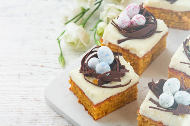 istock Easter carrot cake bars decorated with chocolate nest and chocolate candy eggs blossoming cherry or apple flowers on rustic light wooden backgrounds. Easter holiday meal. Traditional Easter food. 1909822232
