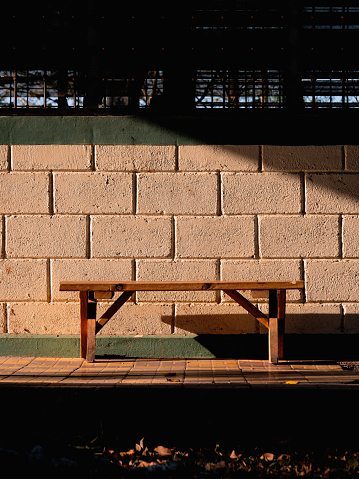 A wooden bench situated next to a wall in the shadows.