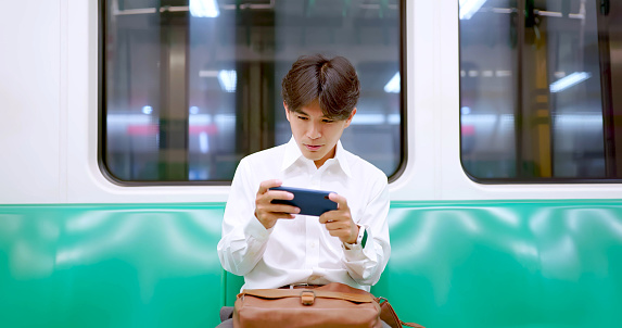 portrait asian happy businessman is playing mobile games while sitting commuting at metro mrt car