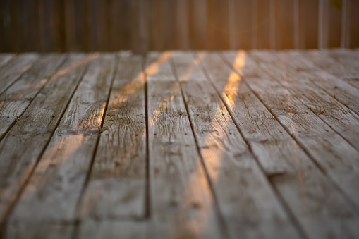 Wooden patio background in the summer evening with copy space for text. Sun rays coming through the rail. Warm image.