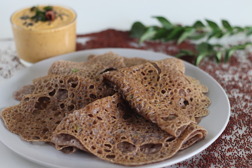 Instant Finger Millet Dosa, made with finger millet flour, curd and spices. Served with coconut chilly condiment. Easy and healthier alternative to rice based fermented crepe. Shot on white background