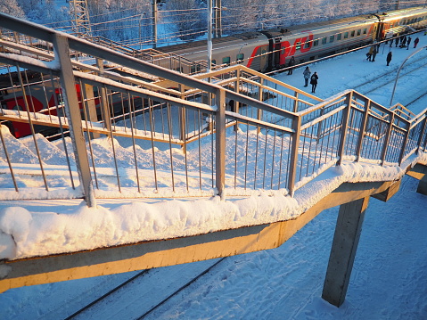 Svir, Russia,01.02.24: Svir railway station on the Oktyabrskaya railway. Passenger freight trains on rails. People and passengers walk along the platform. Winter short polar day. Snow and snowdrifts.