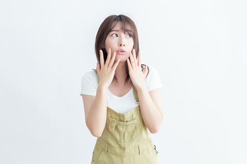 A young woman in a white shirt and green overall looks surprised