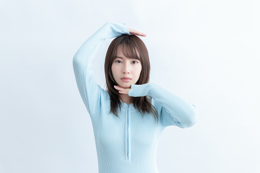 Young Asian woman in blue sweater posing with hands near head