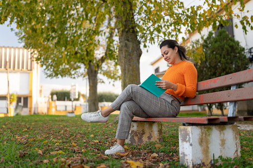 Mature woman reading book sitting on park bench in autumn