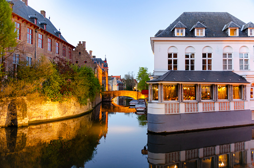 Bruges, Belgium, at twilight, where the evening light brings a magical glow to the city's medieval architecture and reflective canals. The tranquil waters and historic buildings are softly illuminated, enhancing the romantic and timeless atmosphere of this enchanting European gem.