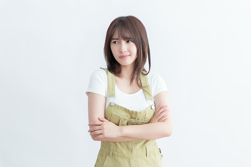 A young woman in a white shirt and khaki overalls is looking away with her arms crossed.