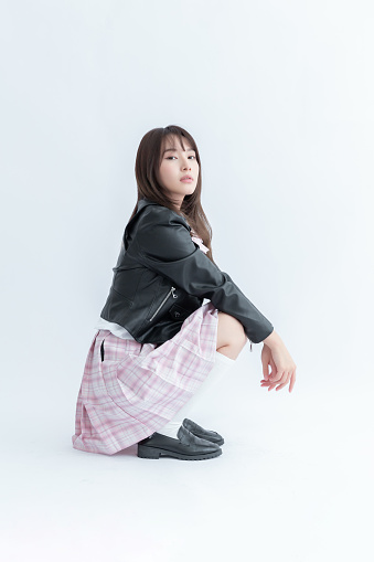 Asian school girl in pleated skirt and leather jacket posing