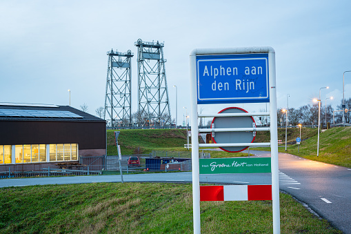 Alphen aan den Rijn, Netherlands - January 4, 2024: Place name sign of the town of Alphen aan den Rijn with the famous lift bridge over river ¨Gouwe¨ in the background.