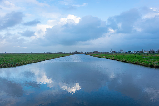 Serene image of clouds reflected in a wide ditch in the plain wide open landscape of The Netherlands.