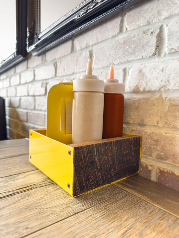 Ketchup and mustard squeeze bottles on top of a wooden restaurant table