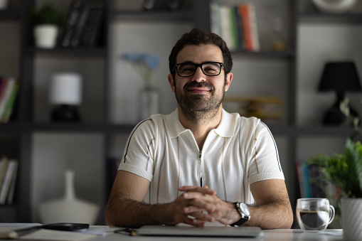 Confident happy businessman in eyeglasses sitting at home workplace and looking at camera.