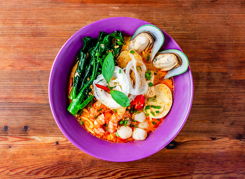 seafood laksa soup with shrimp, prawn, sea shell, noodles and boiled egg served in dish isolated on wooden table top view of hong kong food
