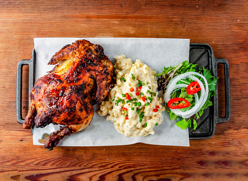 Whole grilled chicken with side dishes mac and cheese served on board isolated on wooden table top view of hong kong food