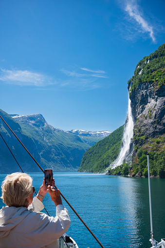 Geirangerfjord, Norway, June 26, 2023: The Seven Sisters waterfall gets its name from, the seven separate streams, the tallest measures 250 meters. A passenger takes photos from the deck of a ferry.