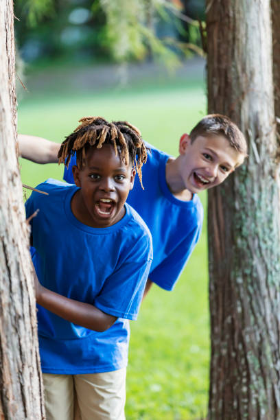 Two boys playing at park, peeking out from behind trees