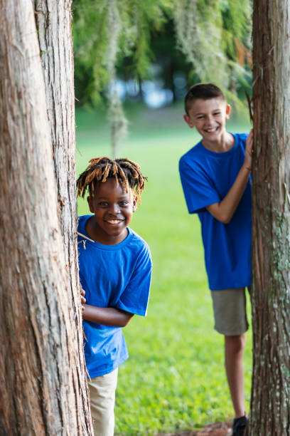 istock Two boys playing at park, peeking out from behind trees 1910259951