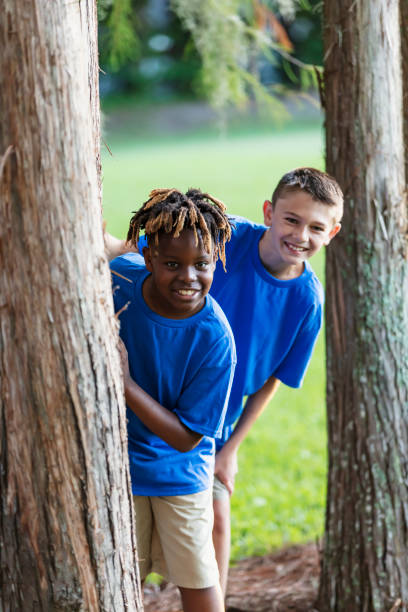 istock Two boys playing at park, peeking out from behind trees 1910259953
