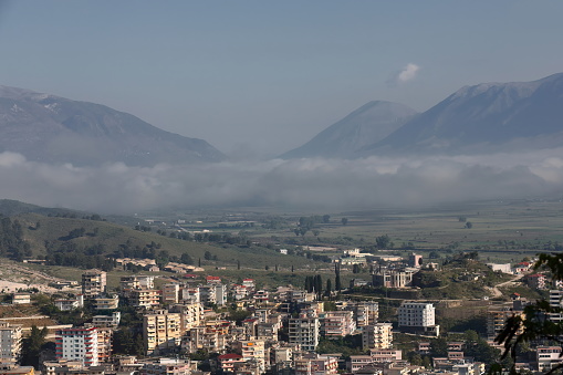 Buildings on the city lower area, fog-covered Drino river valley flanked by Mali i Gjere -left, west- and Lunxheri -right, east- massifs, as seen northward from the city fortress. Gjirokaster-Albania.