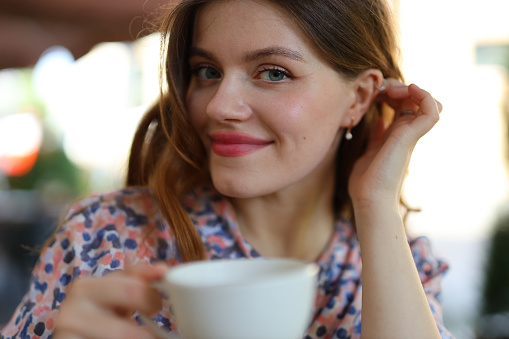 Happy young woman enjoying coffee, pretty portrait, cheerful smile, attractive lady in urban cafe.