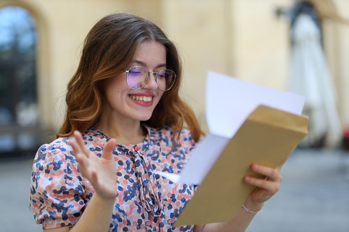 Successful young woman, student or businesswoman, reading mail with a happy smile in a city setting.