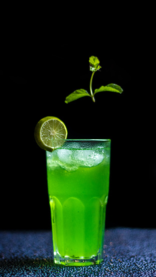 A green beverage with a slice of lime garnish served in a tall glass