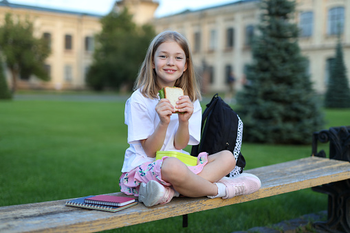 Cool schoolgirl in the park, eating a sandwich, relaxed and happy, enjoying outdoor leisure.