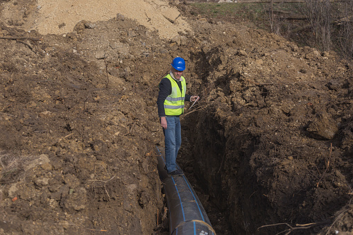 Mature adult inspector controlling quality of works at new plastic pipeline construction site using tablet