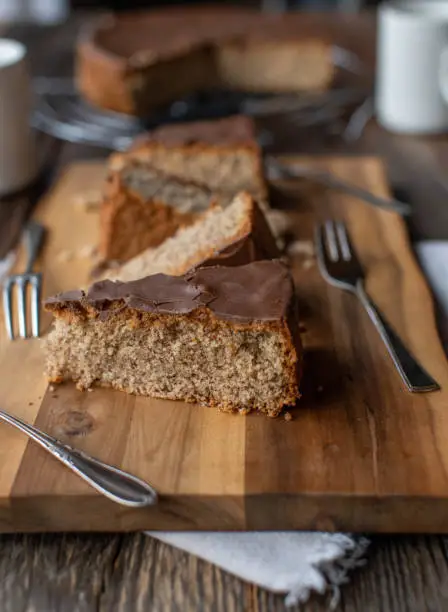 Delicious gluten free almond cake with milk chocolate glaze. Served in slices with forks on wooden table background. Closeup, front view, with copy space