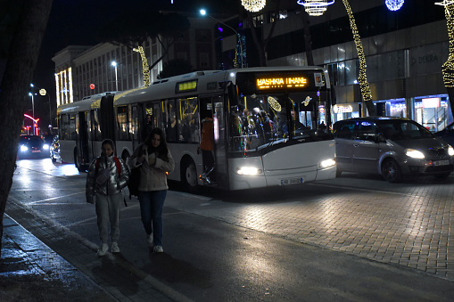 Tirana, Albania - December 21, 2023: Public Transportation Bus, Building Exterior, Road Traffic, People Walking, Christmas Decorations Scene In Tirana City