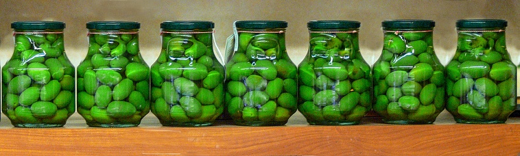 Seven jars of green olives standing neatly in a row on a shelf